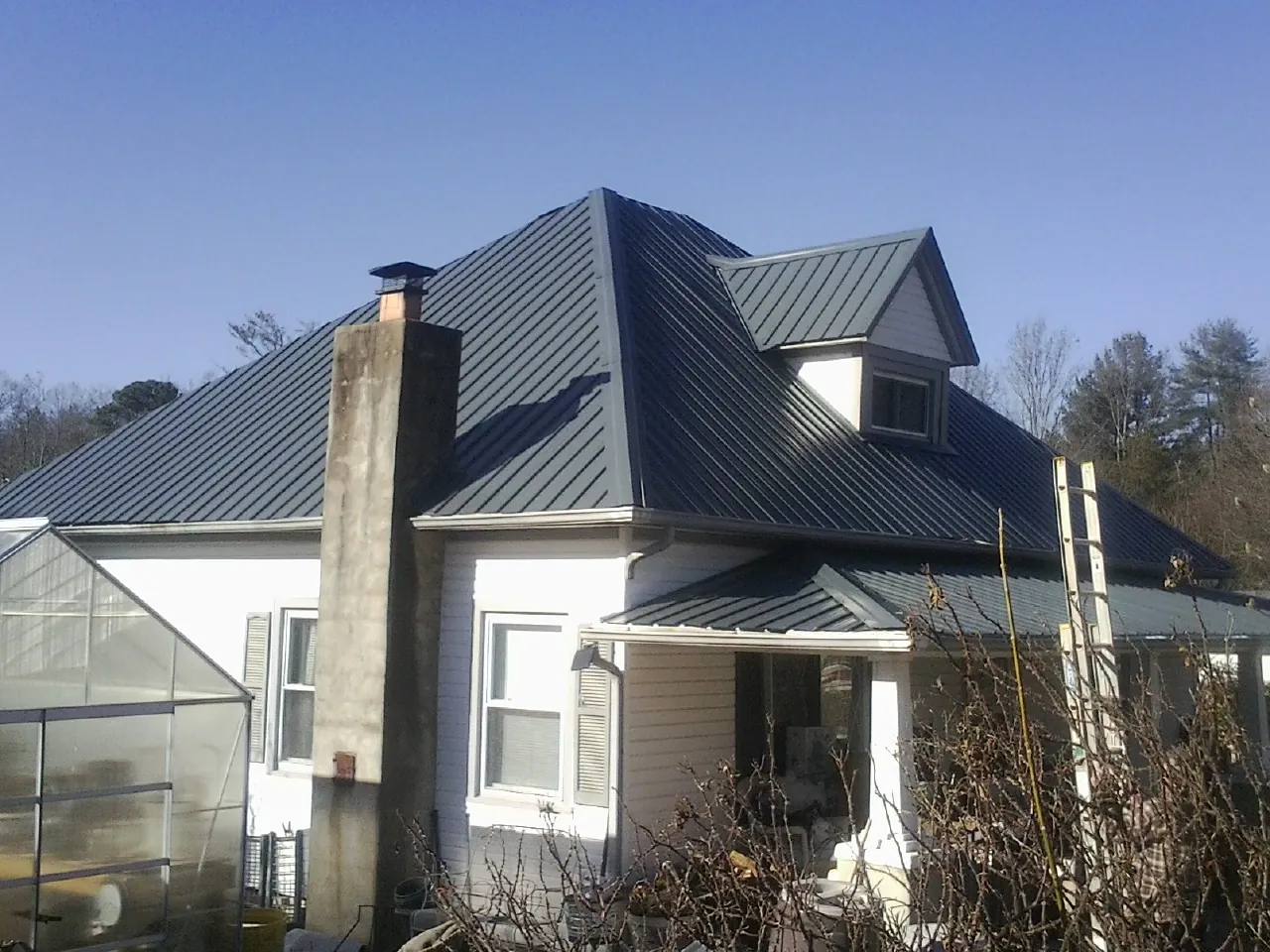 Dark blue standing seam metal roof on a white farmhouse with dormer — Slate & Tile Roof Repair by Roofing Brothers in Bowersville