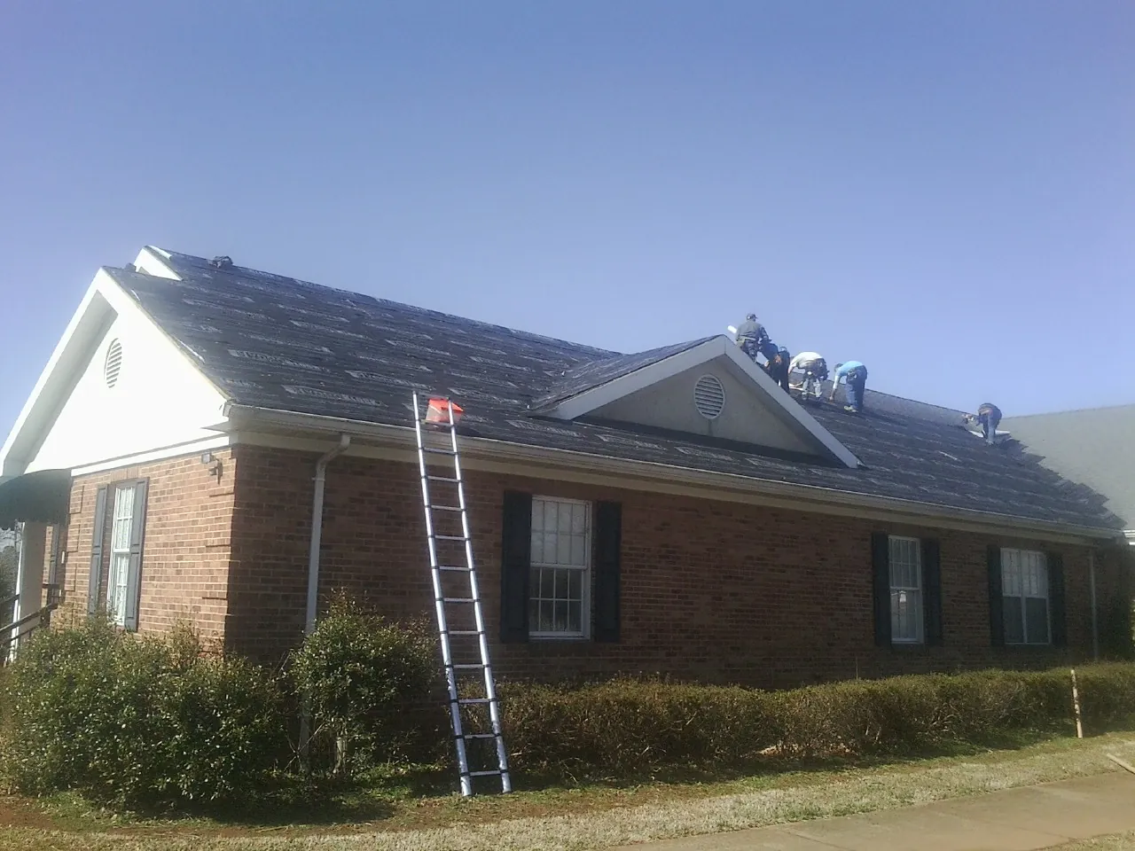 Crew tearing shingles off a brick ranch roof with a ladder set — Metal Roof Repair work by our crew in Bowersville