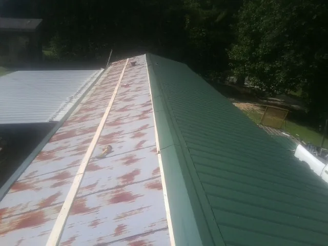 Old rusted panels beside newly installed green metal roofing — Wind Damage Roof Repair by Roofing Brothers in Bowersville