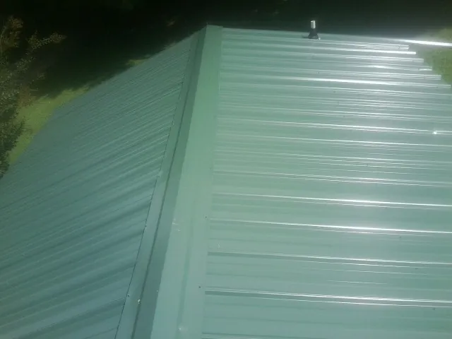 New green metal panels meeting at the ridge of a roof — Flat Roof Repair work by our crew in Bowersville