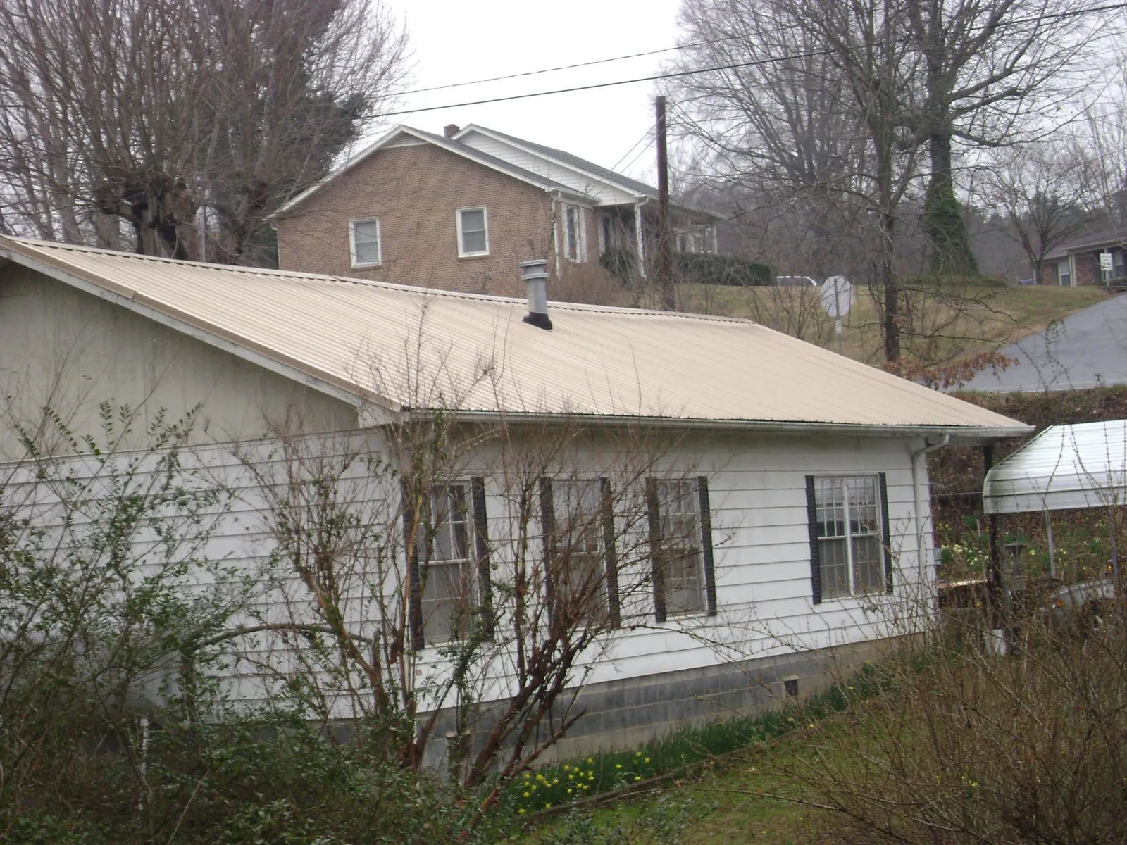 Tan metal roof on a white sided house set into a hillside — Commercial Roofing by Roofing Brothers in Bowersville